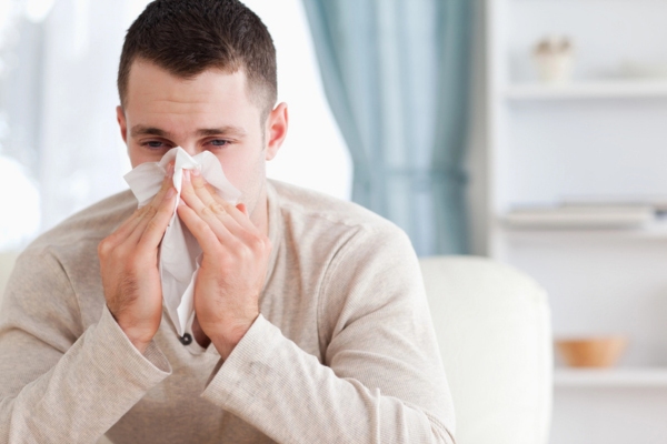 man on the couch sneezing depicting leaking HVAC ductwork