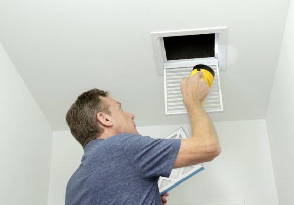 homeowner holding a flashlight while inspecting home air ducts