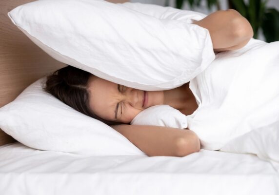 woman covering ears with pillow due to furnace sounds